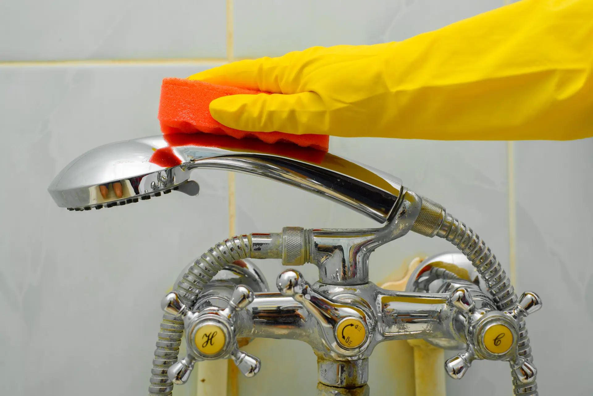 An Urgent Pro cleaner kneeling beside a Brisbane rental bathtub, scrubbing the tile surrounds and cleaning the tapware with a scrubbing brush and bathroom cleaner while the mirror above reflects the clean state of the room