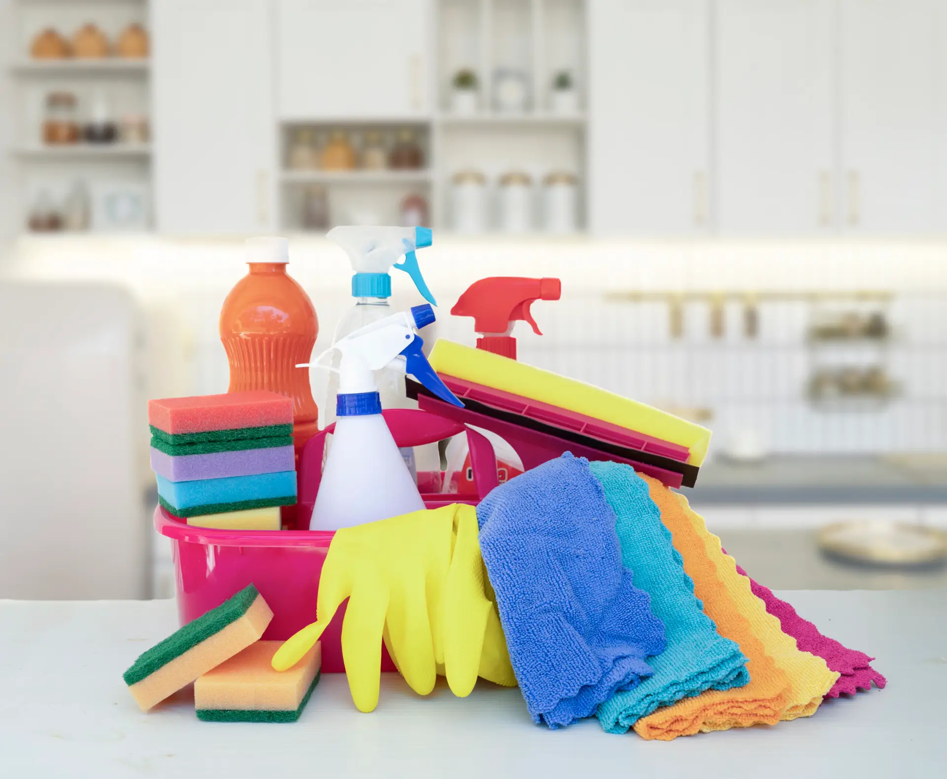 A selection of Urgent Pro vacate cleaning products and tools arranged on a Brisbane rental kitchen bench including a mop and bucket, a vacuum, multipurpose spray, glass cleaner, oven cleaner, rubber gloves and microfibre cloths in different colours