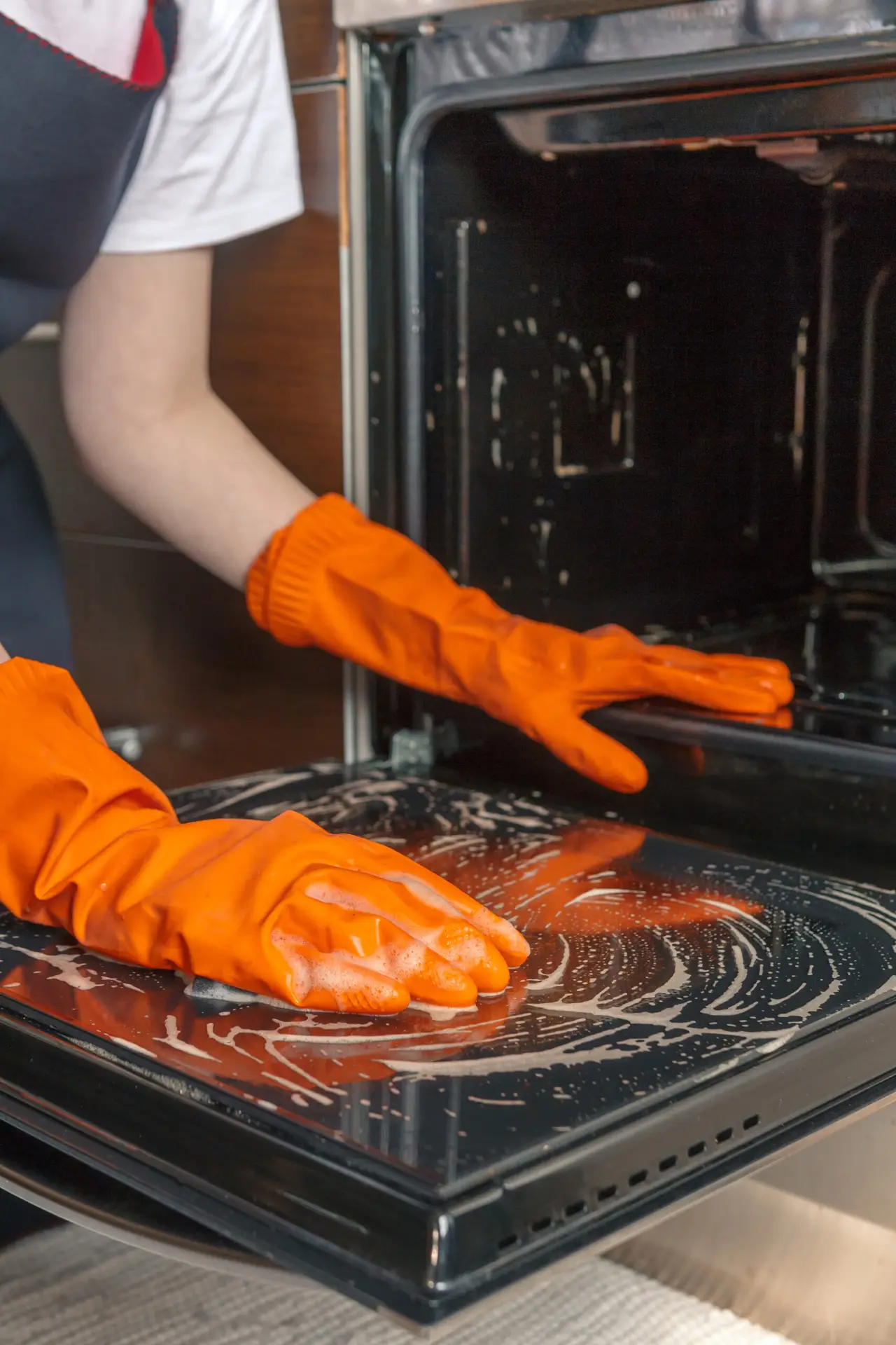 An Urgent Pro cleaner at a Brisbane rental removing the oven racks and placing them in a sink of hot water and degreaser, while the oven interior walls are sprayed with oven cleaner and left to soak before scrubbing