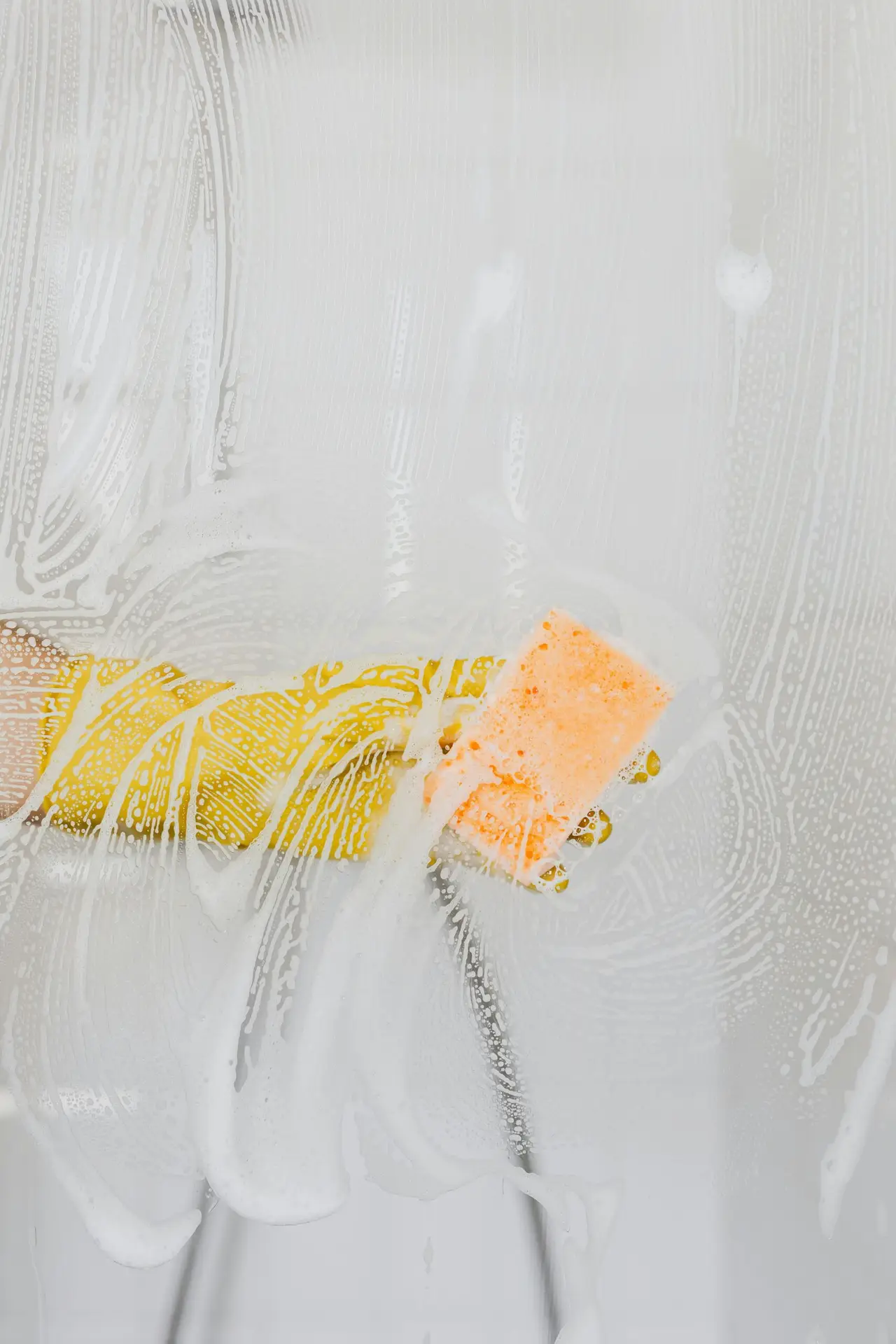An Urgent Pro cleaner polishing chrome tapware and scrubbing grout between the floor tiles of a Gold Coast rental bathroom, with a scrubbing brush, chrome polish and grout spray visible on the vanity shelf beside the clean sink