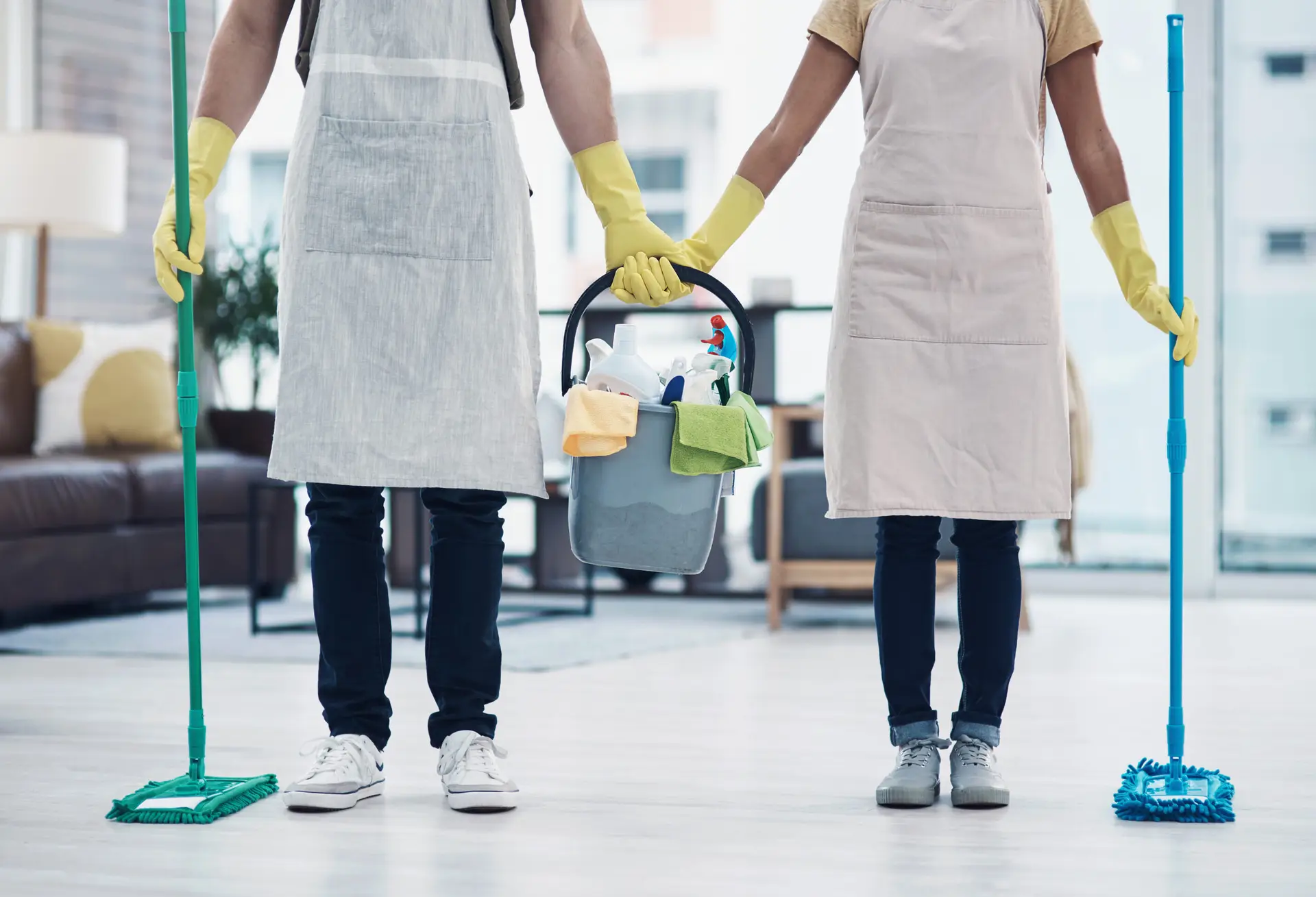 An Urgent Pro cleaner arriving at a Gold Coast rental property in the morning, carrying a well-organised cleaning caddy and a mop, with the Gold Coast residential street and tropical plants visible in the background behind the open front door