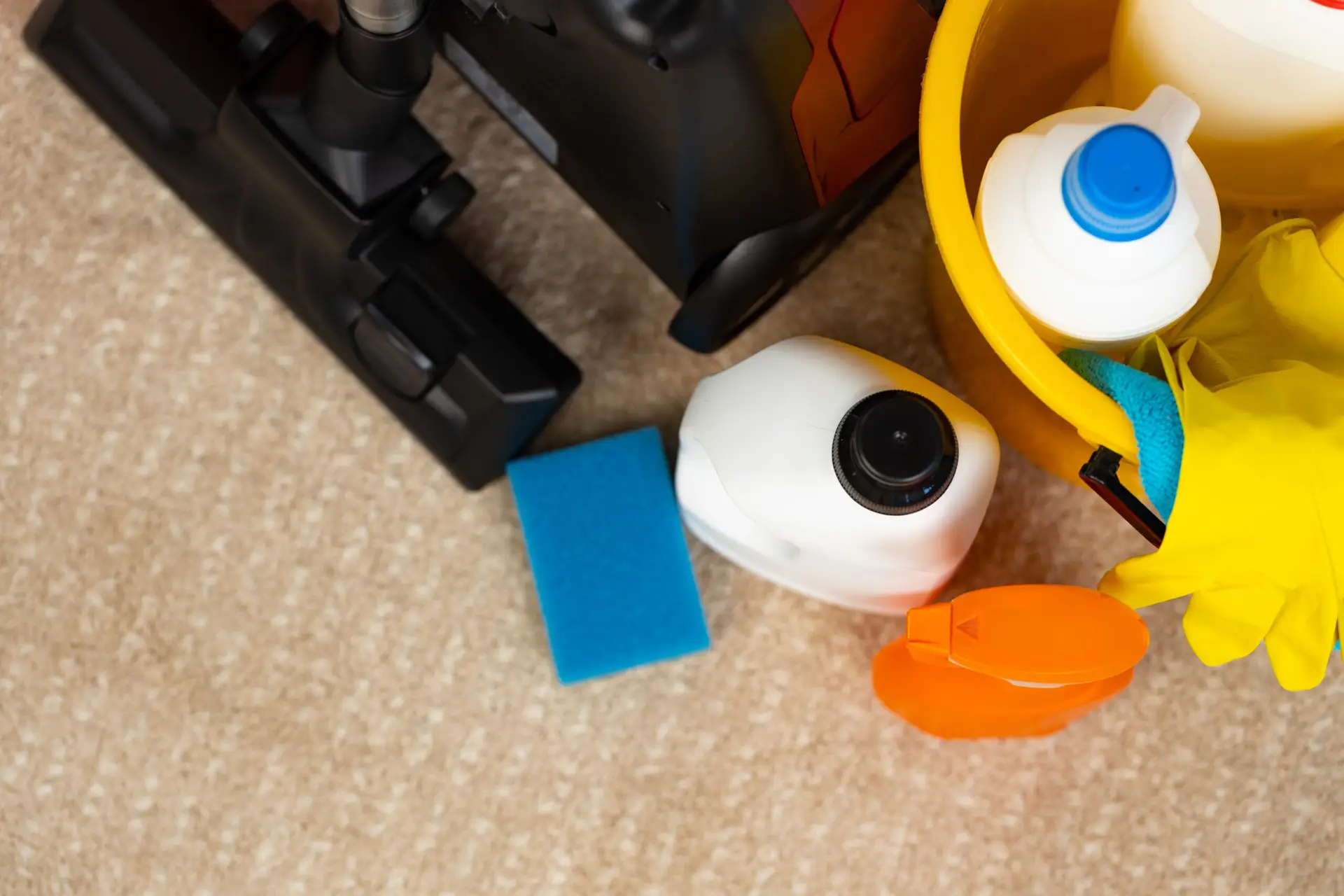 Professional vacate cleaning supplies arranged on the floor of a Gold Coast rental entry — vacuum cleaner, steam mop, a caddy of spray bottles, rubber gloves, grout brush, microfibre cloths and oven cleaner in preparation for a complete rental clean