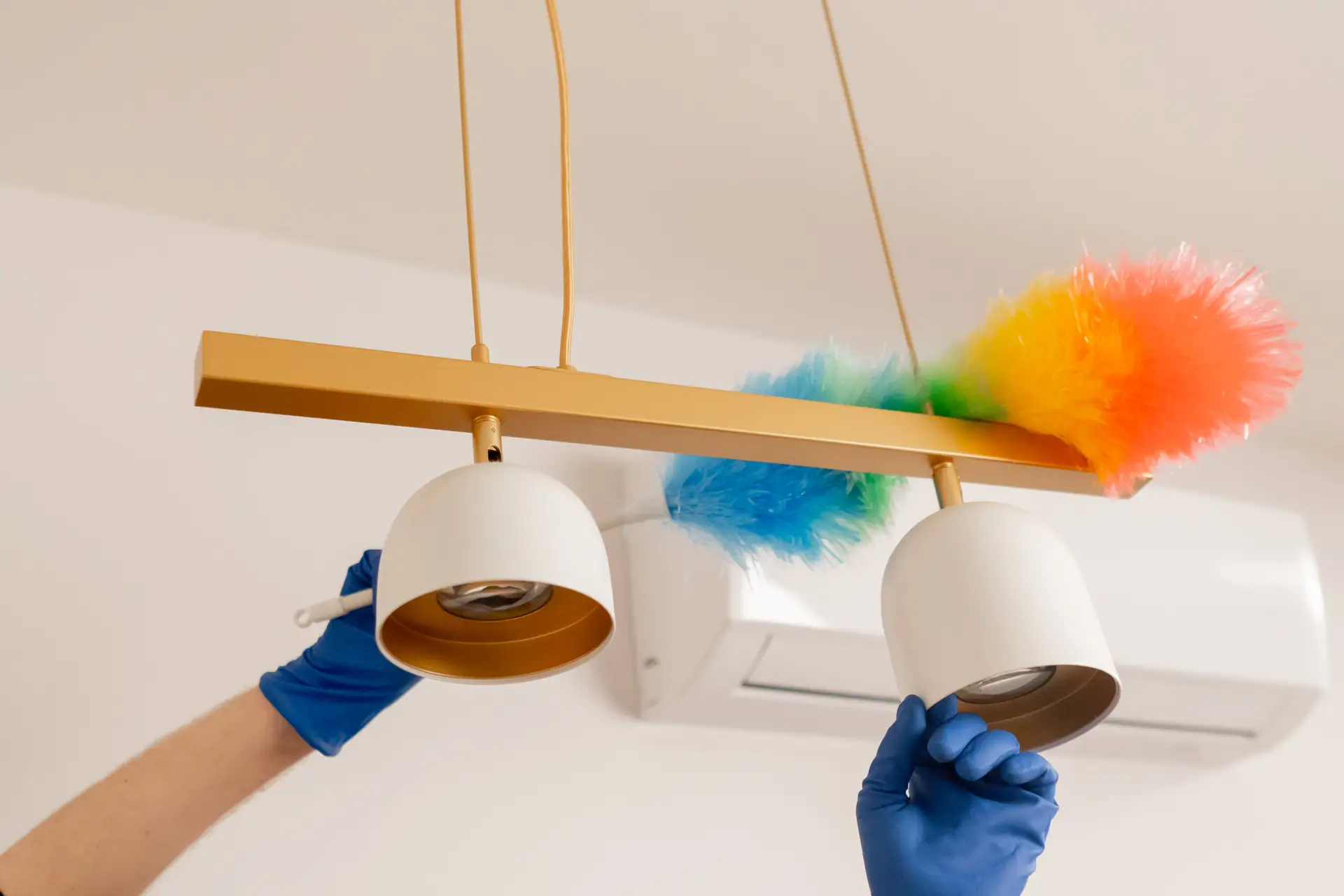 An Urgent Pro cleaner using an extendable duster to clean ceiling corners and the top of the architrave in a vacant Melbourne rental living room, with late afternoon light coming through the large windows behind them