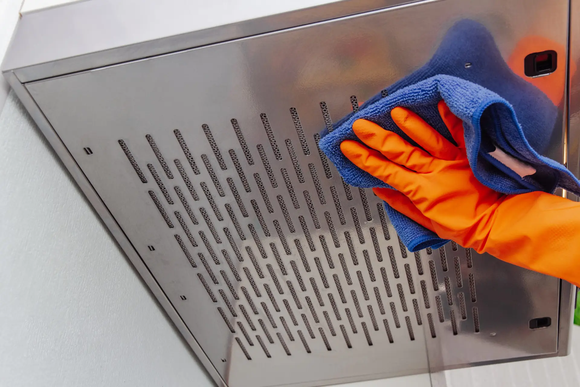 An Urgent Pro cleaner removing the metal filter from a rangehood above a Melbourne rental kitchen stovetop and submerging it in a sink of hot degreaser solution, with the cleaned filter resting on a cloth beside the sink