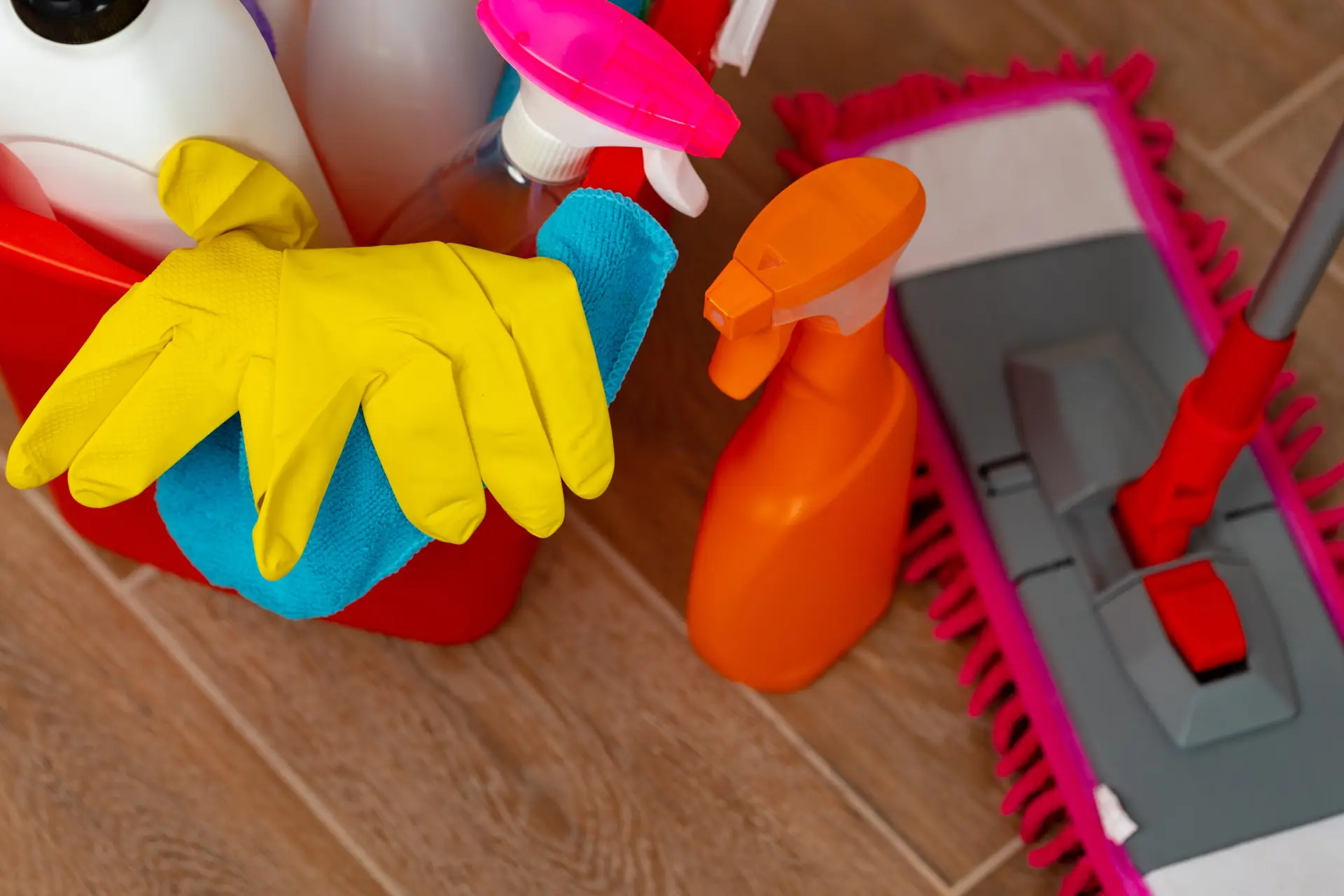 Vacate cleaning supplies organised in a row on the floor of a Melbourne rental entry — including a steam mop, vacuum cleaner, glass cleaner, surface spray, oven cleaner, rubber gloves and microfibre cloths in multiple colours