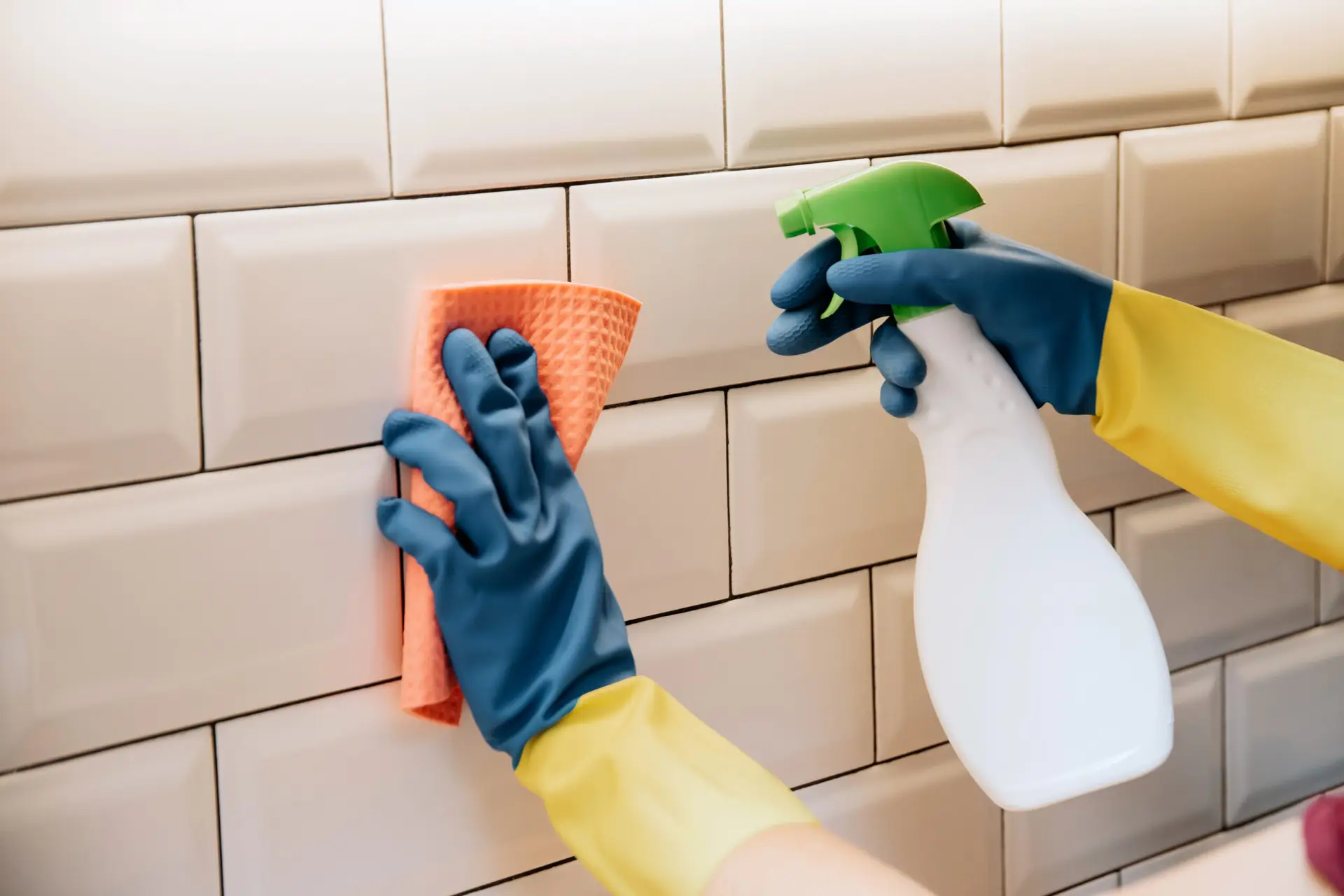 An Urgent Pro cleaner scrubbing grout lines between floor tiles and polishing the shower screen glass in a Sydney rental bathroom, with a grout brush, spray cleaner and microfibre cloth visible on the tile shelf beside them