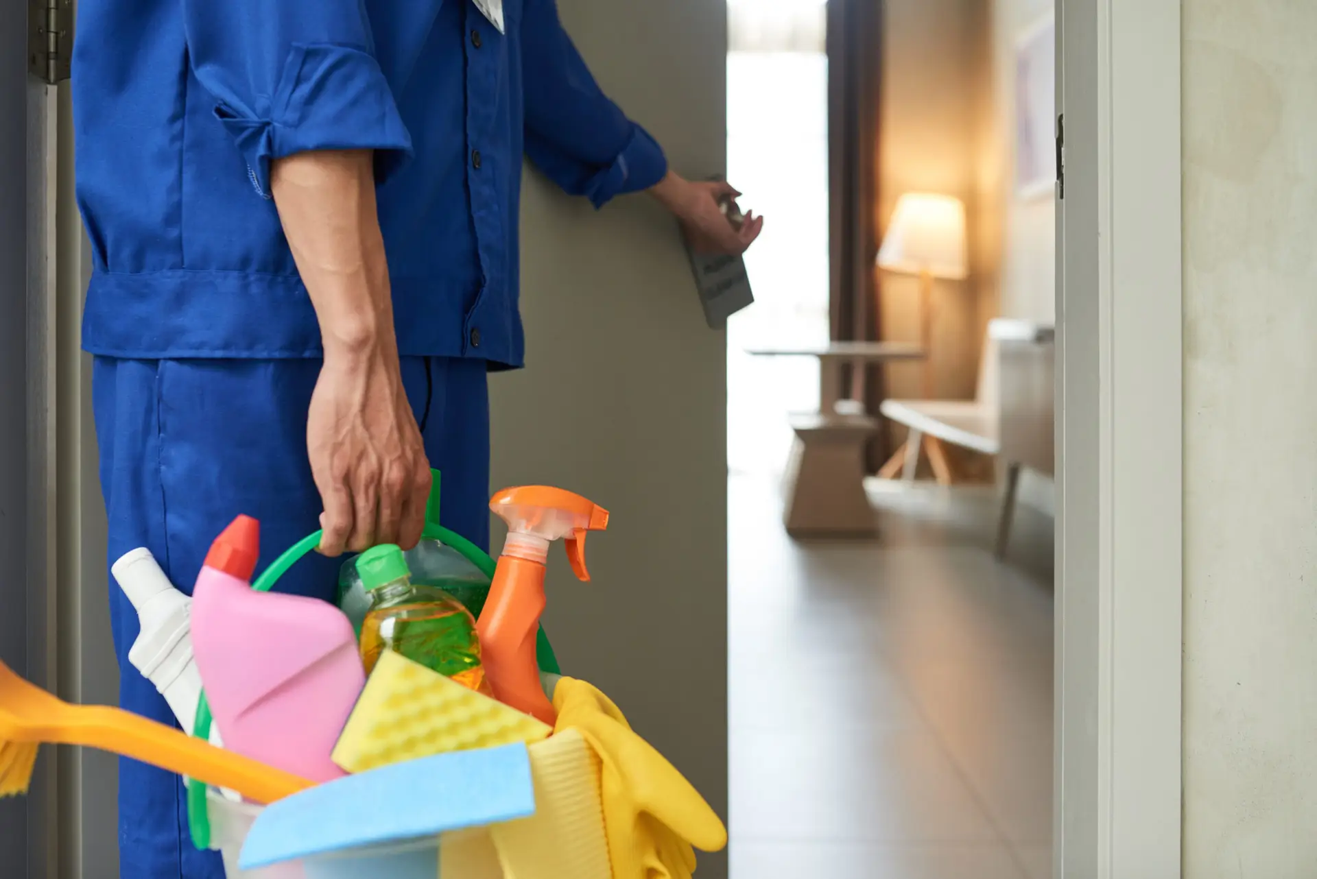 An Urgent Pro cleaner standing at the front door of a Sydney rental property, holding a full cleaning caddy and a mop, about to begin a vacate clean for a tenant who is handing over the keys